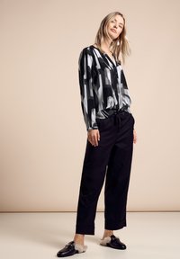 Blouse à motif noir et blanc avec des détails de boutons, associée à un pantalon noir ample et des chaussures noires avec un accent duveteux.