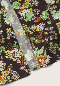 Tissu foncé avec un motif floral vert, jaune, blanc et orange, présentant des bords cousus et une section pliée semi-transparente.