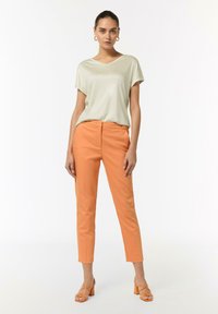 Jasnozielona bluzka z krótkim rękawem, dekolt w serek; pomarańczowe spodnie slim-fit; pomarańczowe sandały na blokowym obcasie; minimalistyczny design z gładkimi teksturami.