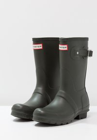 Grüne Gummiregenstiefel mit matter Oberfläche. Mit einem Logo-Patch am Schaft und einer Schnallenakzentuierung an der Außenseite. Strukturierte Sohle.