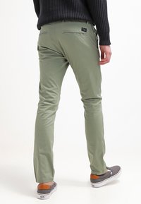 Ljusgröna byxor i bomull med en slät yta. Har fickor och en figurnära passform. Matchas med grå skor och en orange accent.