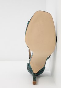 Korkokenkä, jossa on teksturoitu turkoosi ulkopinta, suljettu kärki ja ohut korko; vaaleansävyinen pohja uritetulla kuvioinnilla pitävyyttä varten.