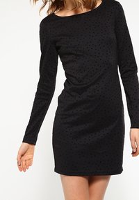 Czarna sukienka z długim rękawem i okrągłym dekoltem, z teksturowanymi kropkami, dopasowaną sylwetką i miękkim materiałem.