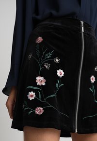 Zwarte fluwelen rok met bloemenborduurwerk in roze en wit, met een voorrits en een getailleerd ontwerp.
