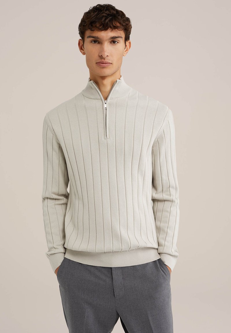 Pullover deschis la culoare, cu fermoar, cu textură cu nervuri, are o guler înalt și manșete ajustate. Purtați peste pantaloni gri închis.