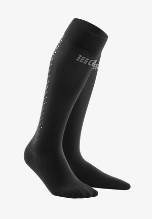 Calze compressive nere al ginocchio con bordo a coste, grip testurizzato nella zona del piede e un motivo di croci bianche lungo il lato per un tocco di dettaglio in più.