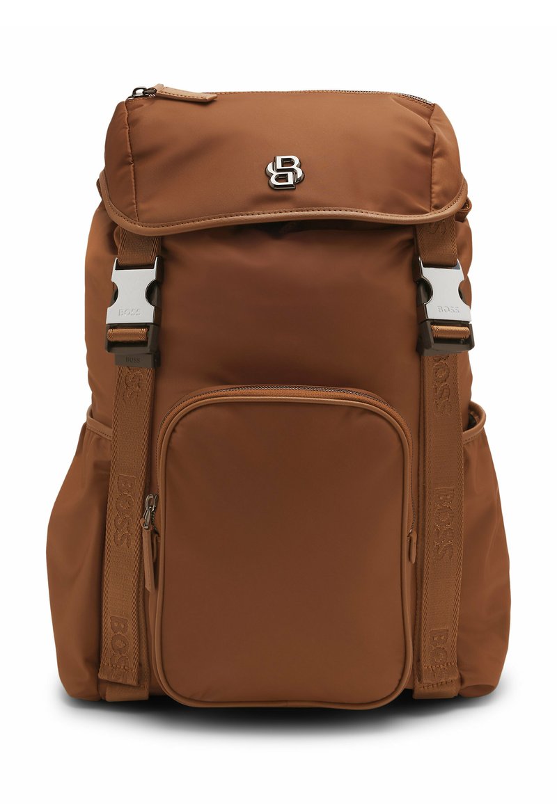 Brązowy plecak z nylonu z regulowanymi paskami, przednią kieszenią na zamek i klapą. Posiada metalowe okucia i detal z logo.