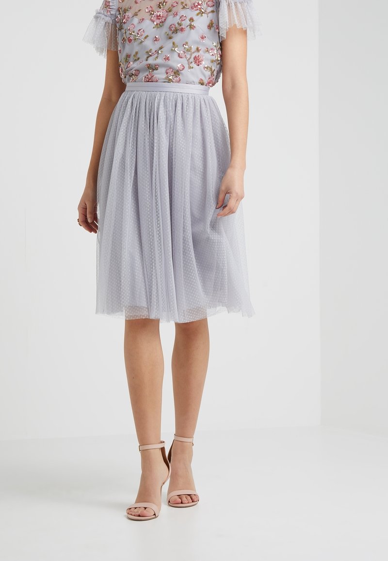 Falda de tul gris claro con lunares, con una cinturilla ajustada. Combinada con una blusa adornada con flores y tacones de cinta al tobillo en tono nude.