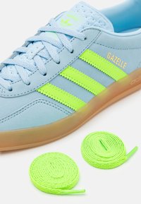 Sneaker in suede azzurro chiaro con strisce verde neon, dotato di linguetta testurizzata e due paia di lacci coordinati. Suola in gomma con una leggera trasparenza.