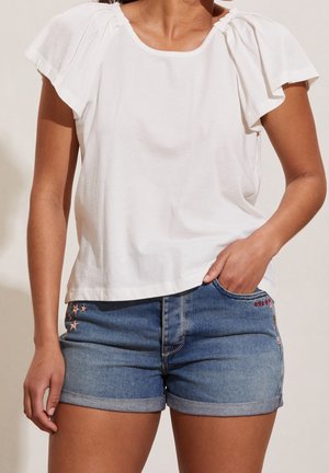 T-shirt en coton blanc avec des manches volantes, associé à un short en denim orné de broderies en forme d'étoile et de cœur à l'avant.