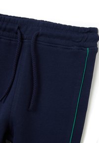 I pantaloni tuta navy presentano una vita con coulisse, una texture liscia e una striscia laterale verde per contrasto. I polsini elastici completano il design.