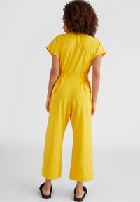 Gul byxdress med korta ärmar, elastisk midja och sidofickor. Vid ben-design med ett mjukt, lätt tyg och enhetlig färg.