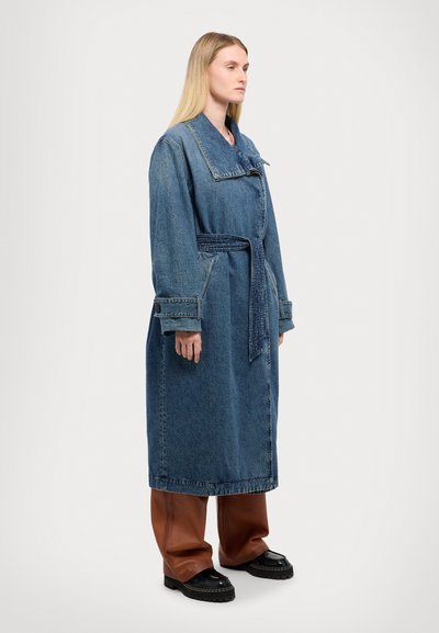 Denimjakke med bælte i taljen, bred krave og lange ærmer. Har en blå vaske, synlig syning og en løs, oversized pasform.