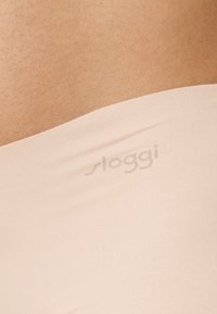 Sloggi naadloze ondergoed in licht perzik stof, met een gladde textuur, elastische band en subtiele branding in een tonale print.