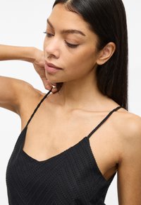 Čierna kamarátka s nastaviteľnými ramienkami vo forme špagiet, s textúrovaným cik-cak vzorom. Hladká látka s priliehavým strihom.