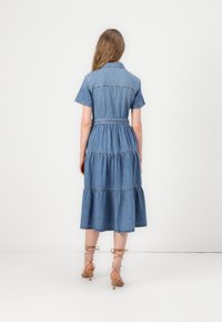 Robe en denim à manches courtes, jupe à volants et taille ceinturée. Couleur bleu clair, détail de col et accents de couture discrets.