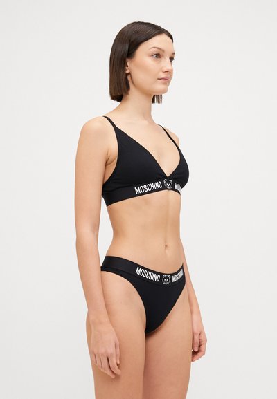 Black bikini set featuring a triangular bralette and low-rise briefs, both adorned with a white Moschino logo band. Smooth texture.