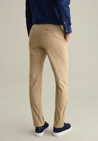 Khaki broeken gemaakt van lichtgewicht stof, met een slim fit, achterzak met knoop, en gecombineerd met zwarte schoenen.
