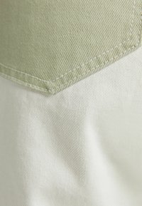 Tejido verde claro y crema con una textura suave y costuras contrastantes, mostrando una costura diagonal a lo largo de la superficie.