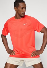 Κόκκινη αθλητική μπλούζα με υφή, στρογγυλή λαιμόκοψη και κοντά μανίκια. Διαθέτει το λευκό λογότυπο της Nike στο στήθος.