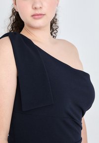 One-shoulder navy dress made of smooth fabric, featuring a draped shoulder detail and a fitted silhouette.