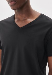 T-shirt nero in cotone con scollatura a V, maniche corte e una texture liscia, con cuciture minime e un taglio aderente.