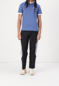 Modré tričko s krátkým rukávem s bílým lemováním, doplněné černými kalhotami se šedými bočními panely a béžovými botami.