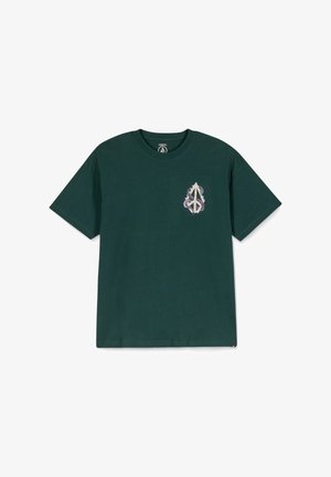 Dunkelgrünes Baumwoll-T-Shirt mit kurzen Ärmeln, das auf der linken Brust ein kleines, aufwendiges grafisches Motiv in Lila und Weiß zeigt.