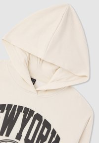 Felpa color crema con una grande scritta nera "NEW YORK" sul davanti. Il tessuto sembra morbido con una vestibilità classica e rilassata, e un cappuccio con cordino.