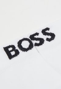 Biele ponožky s čiernym logom "BOSS" na leme. Materiál je z bavlneného zmesi, hladká textúra a dizajn s štandardnou dĺžkou po členky.