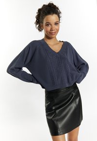 Maglione in cotone spesso di color blu navy con scollo a V, abbinato a una mini gonna in pelle nera aderente.