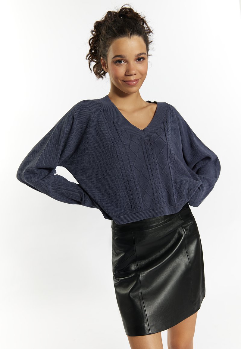 Maglione in cotone spesso di color blu navy con scollo a V, abbinato a una mini gonna in pelle nera aderente.
