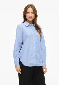 Sinivalkoraidallinen pitkähihainen kauluksellinen nappipaita, jossa on kaareva helma ja rento istuvuus, valmistettu kevyestä kankaasta.