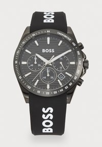 Black chronograph watch with a textured black dial, silver accents, and a rubber strap featuring white "BOSS" lettering. Date display at 6 o'clock.