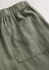 Green linen shorts featuring an elastic waistband, a single patch pocket on the back, and a textured, breathable fabric.