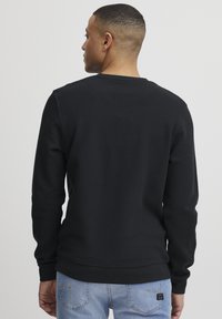 Schwarzes Langarm-Sweatshirt mit strukturiertem Muster, gerippten Bündchen und rundem Ausschnitt, kombiniert mit hellblauen Jeans.