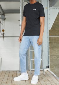 Svart kortärmad polo-shirt med knäppning vid halsen och vit logotyp, som matchas med ljusblå raka jeans och vita sneakers.