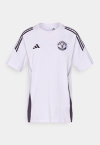 Bílé sportovní tričko s krátkými rukávy s černými akcenty, logem Adidas, znakem Manchester United na hrudi a detaily na bočních panelech.