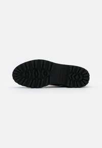 Semelle de botte noire avec des crampons profonds et un motif géométrique, taille 37 marquée sur la zone du talon.