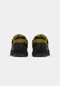 Pár olivovo zelených a čiernych bežeckých topánok s červenými logami Nike, zobrazené zozadu na bielom pozadí.
