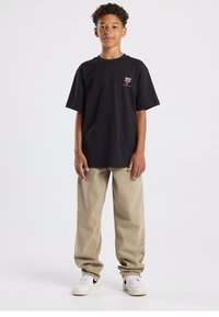 Camiseta negra de algodón con cuello redondo y mangas cortas, con un logo gráfico en el pecho izquierdo. Combina con pantalones sueltos beige.