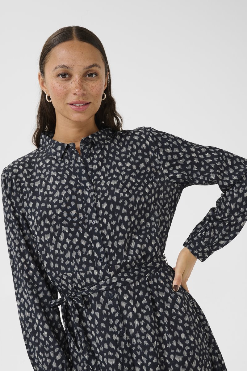 Robe bleu marine à boutons, avec un motif abstrait clair, des manches longues, une taille nouée et une jupe évasée. Tissu doux et texturé.