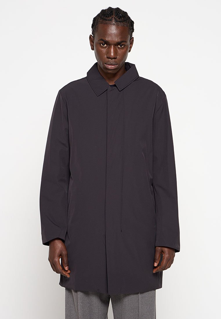 Długi, ciemnoszary płaszcz o prostym kroju, z dużym kołnierzem i gładkiego, wodoodpornego materiału; posiada zapięcie z przodu i brak widocznych kieszeni.