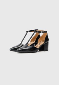 Scarpe con tacco alto in pelle nera con punta affusolata e design a T-strap. Tacco spesso, texture liscia e soletta beige con branding.