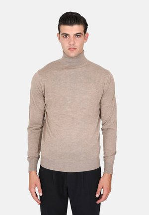 Maglione beige a collo alto realizzato in morbido materiale, con un design aderente, maniche lunghe e polsini a coste. Abbinato a pantaloni neri.