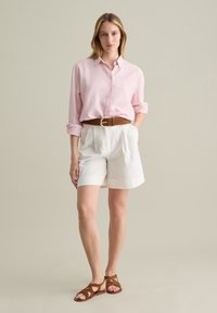 Light pink linen button-up shirt, white pleated shorts, brown leather belt with a circular buckle, and brown strappy sandals.