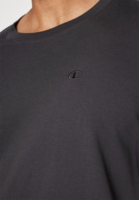Sort kortærmet T-shirt med rund hals. Lavet af blødt stof med et subtilt broderet logo på venstre bryst. Glat tekstur.