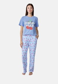 T-shirt di cotone azzurro chiaro con grafica di ciliegie e testo. Pantaloni del pigiama a scacchi con ciliegie e gambi verdi su uno sfondo blu.