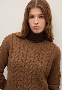 Brown knitted sweater featuring a cable pattern on the front, ribbed crew neckline, and long sleeves with a textured finish.