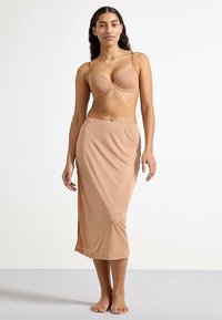 Nude-farbener BH und passender Midirock, beide aus glattem, dehnbarem Material. Der Rock hat einen seitlichen Schlitz für bessere Bewegungsfreiheit.